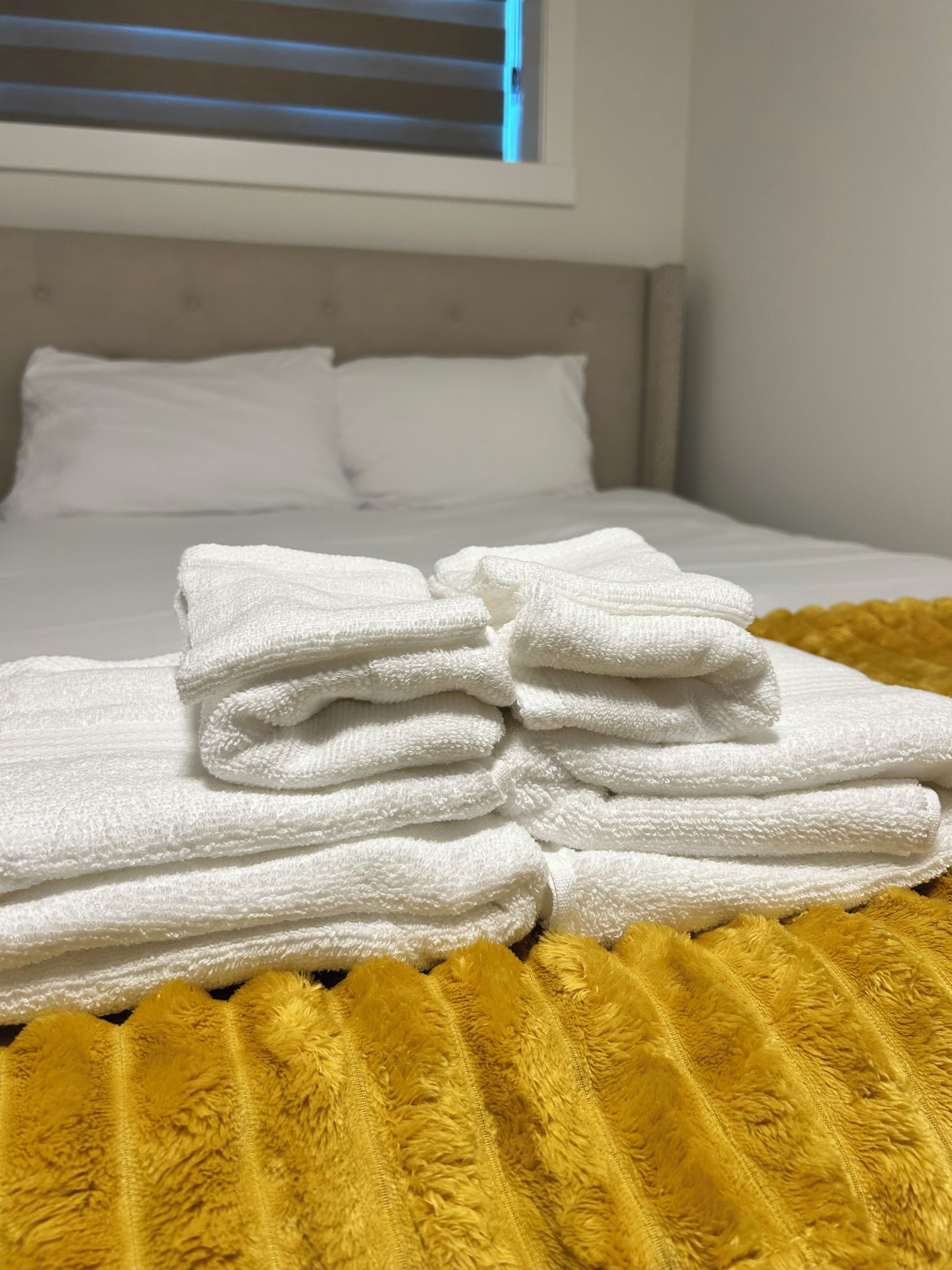 Ein ordentlich bezogenes Bett mit weißen Bettwäsche und einer gelben, flauschigen Decke.