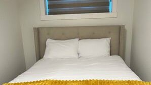 Una cama con cabecera, ropa de cama blanca y una manta amarilla.