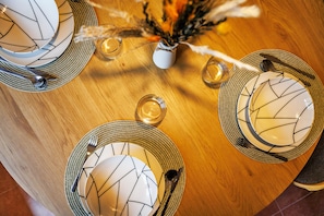 Une table de salle à manger ronde, ornée d’un vase blanc, d’un arrangement de plumes et d’un verre d’eau.