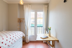 Une chambre à coucher avec un lit, un bureau, une fenêtre avec des rideaux et une vue sur les bâtiments environnants.