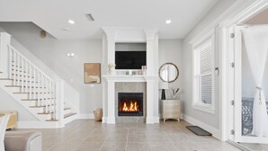 A living room with a fireplace, a staircase, and a door leading to an outdoor area. - 3BR, 3BA, Villa steps from sand with private beach access, beach gear & pool! (Miramar Beach)