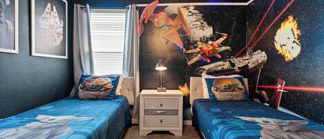 Une chambre avec deux lits, une table de chevet, une fenêtre avec des rideaux et des décorations murales sur le thème de Star Wars.