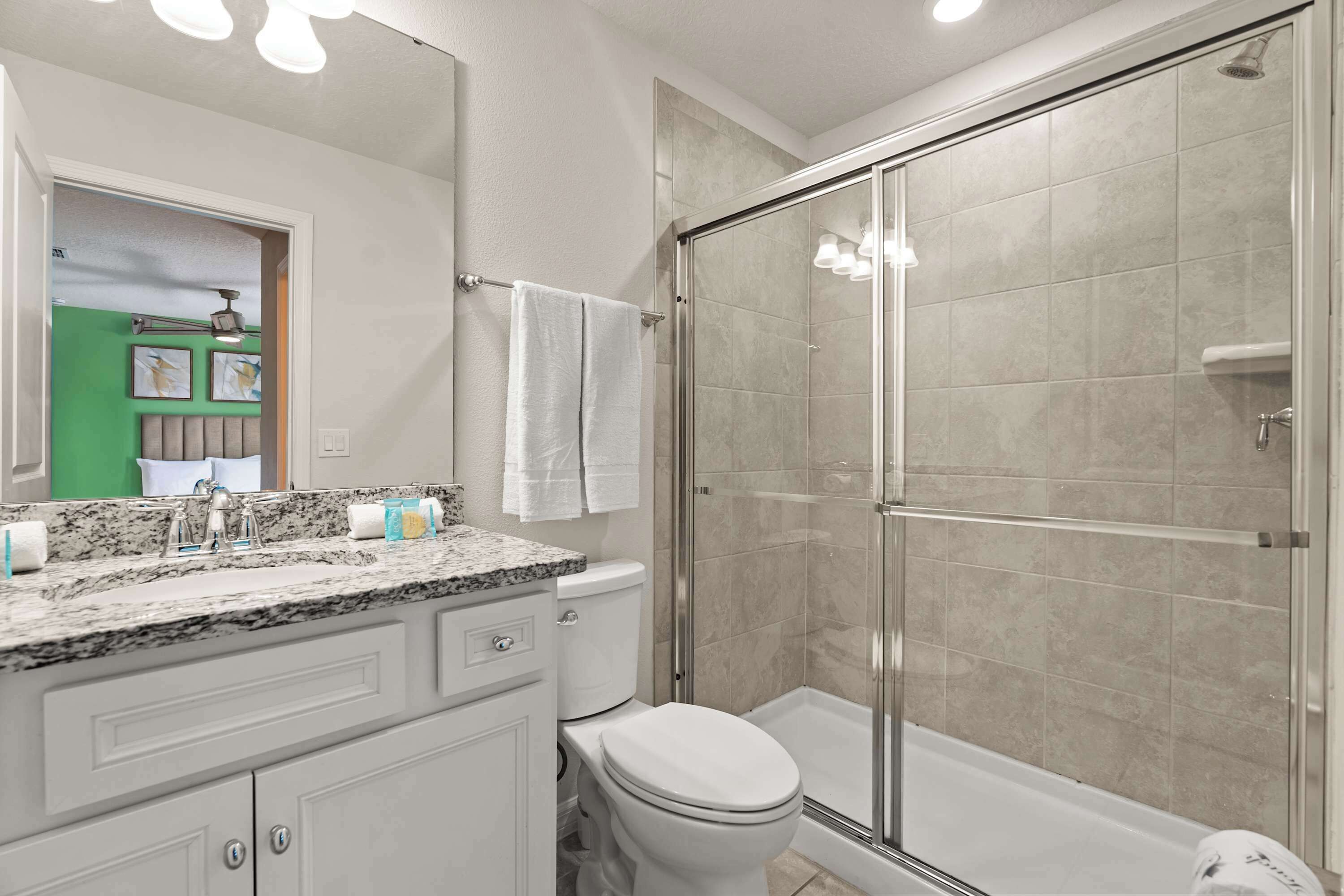 Une salle de bain avec une douche à parois de verre, des toilettes blanches et un comptoir en granit.