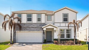 A two-story house with a garage, a front door, and a small front yard with palm trees. - Upstay Disney Family Adventure with Pool & Hot Tub (Davenport)