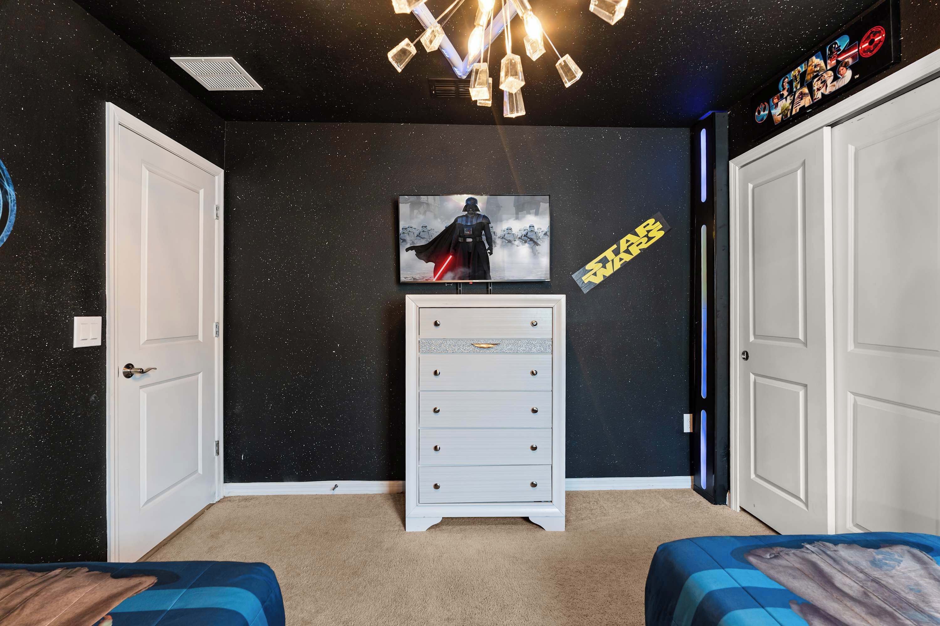 A room with a starry wall, a Darth Vader poster, a Star Wars sign, a dresser, and two beds.
