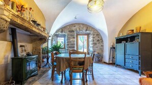 A rustic dining area with a stone archway, wooden table, chairs, and a blue cabinet. - Typical stone house in the middle of a quiet village (MAREUGHEOL)