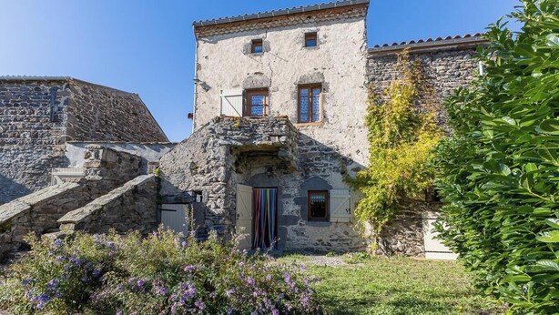 A stone building with a small tower, a wooden door, and a staircase leading to the entrance. - Typical stone house in the middle of a quiet village (MAREUGHEOL)