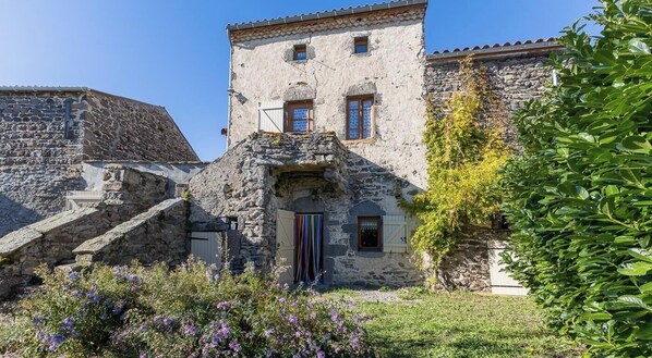 A stone building with a small tower, a wooden door, and a staircase leading to the entrance. - Typical stone house in the middle of a quiet village (MAREUGHEOL)