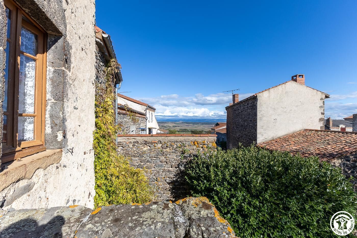 A stone building with a window, a stone wall, and a view of the countryside.
