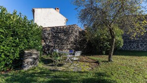 A stone wall, a tree, and a table with chairs in a garden. - Typical stone house in the middle of a quiet village (MAREUGHEOL)