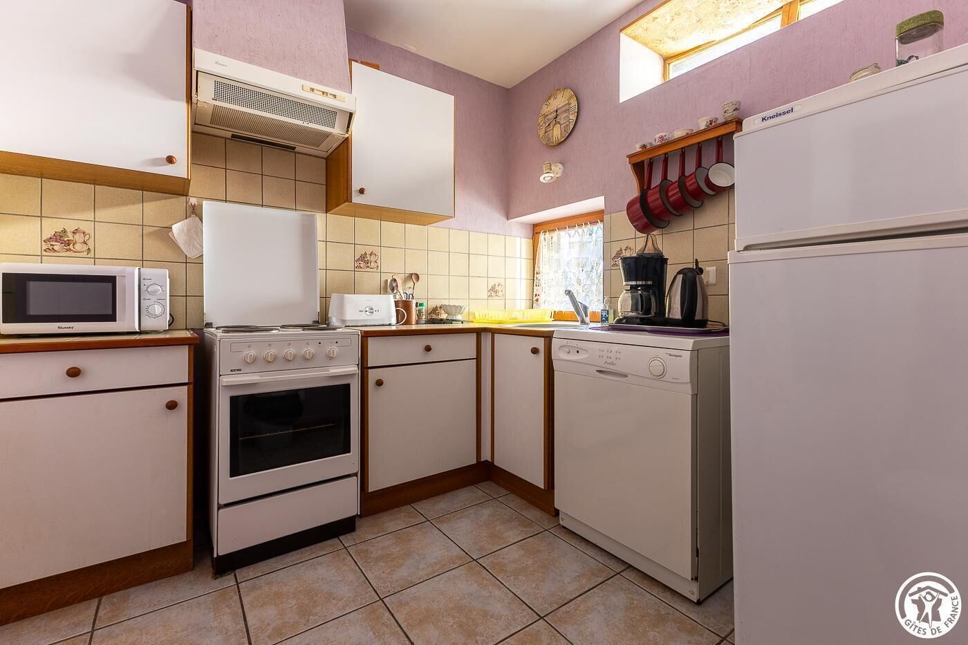 A kitchen with a microwave, stove, oven, dishwasher, and a clock on the wall.