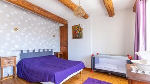 A bedroom with a bed, a crib, a wooden nightstand, a small table, and a purple rug. - Typical stone house in the middle of a quiet village (MAREUGHEOL)