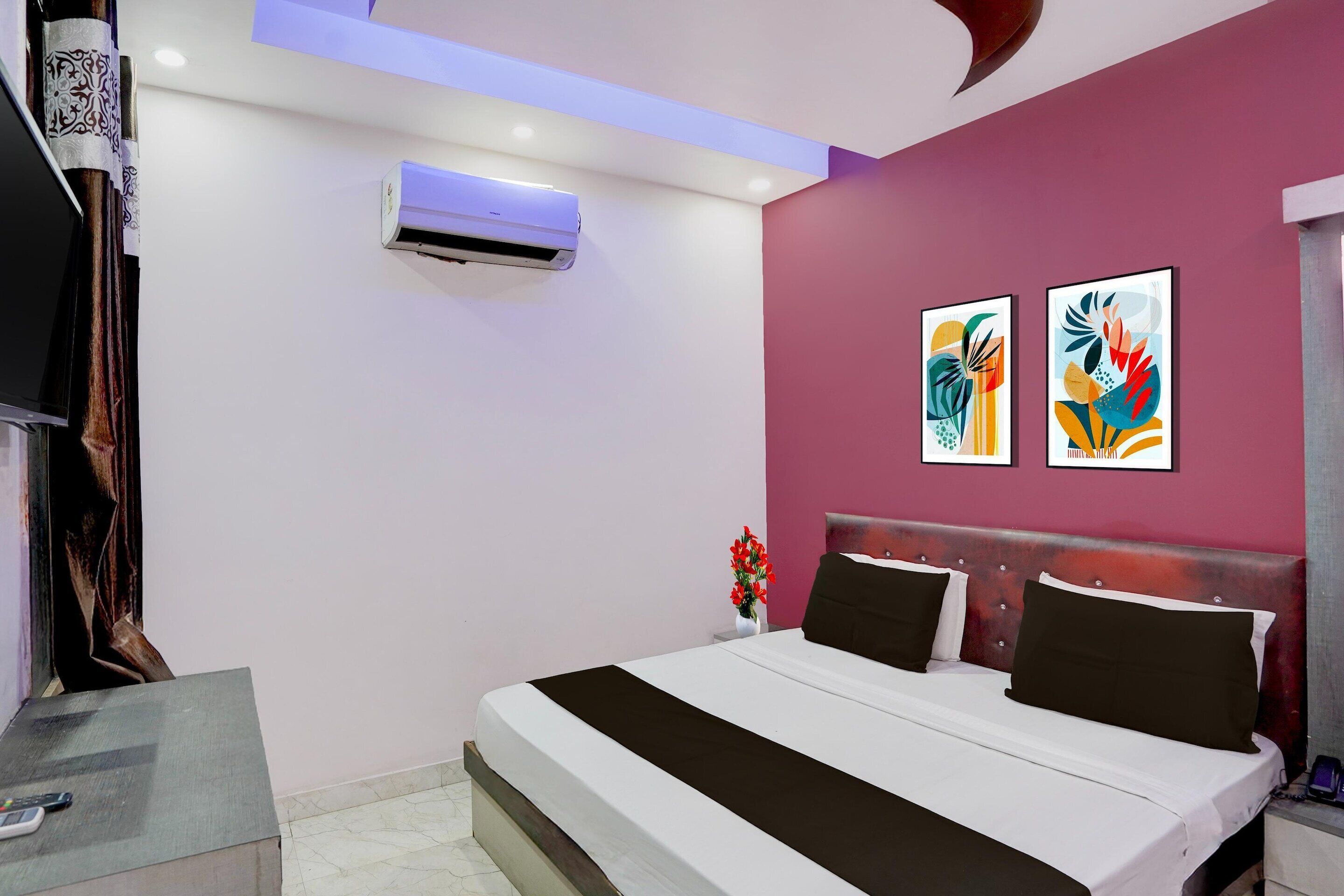 Una moderna camera d'albergo con un letto, condizionatore d'aria, un'opera d'arte e un comodino con un vaso di fiori.