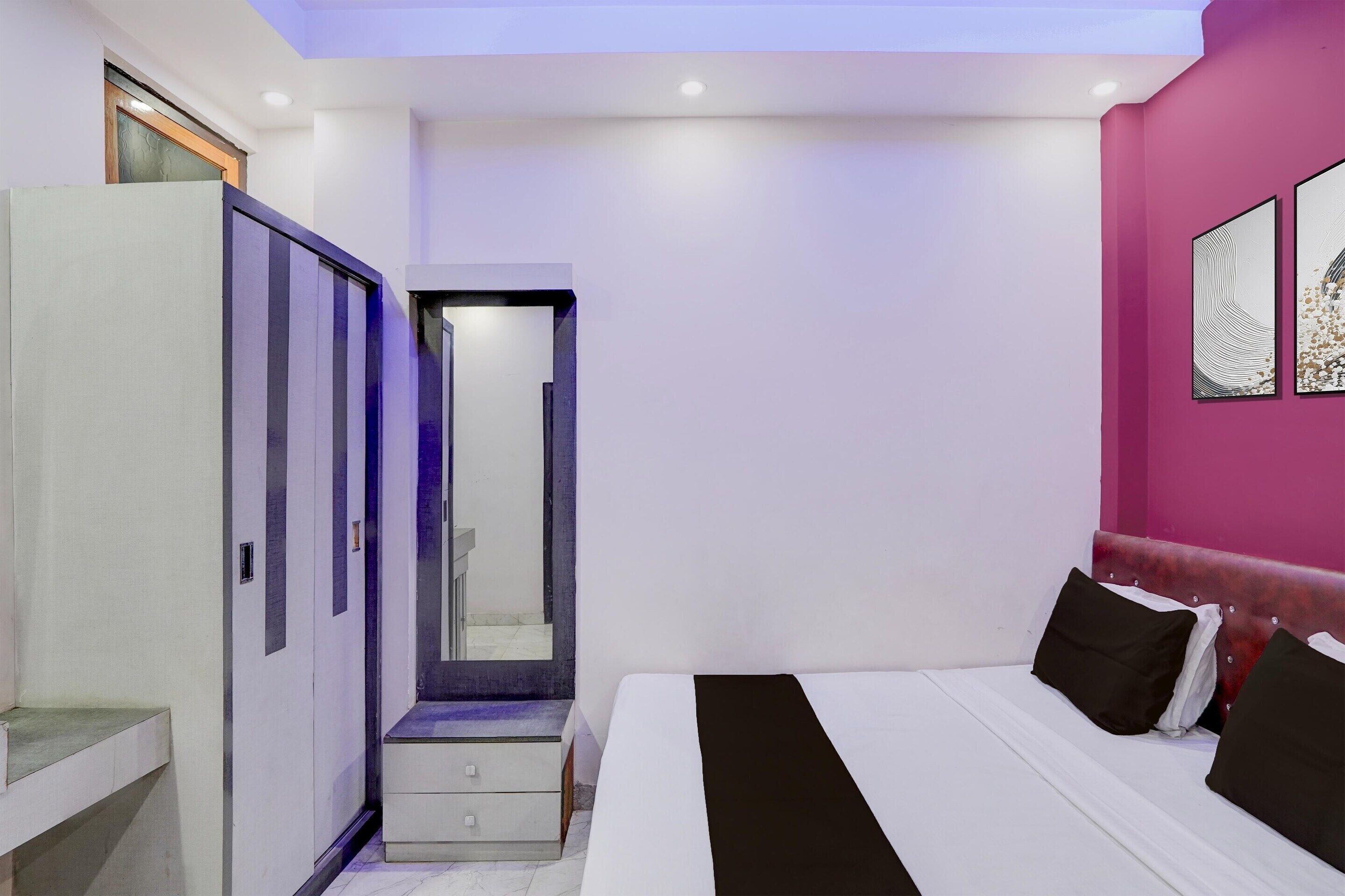 Een slaapkamer met een bed, een garderobe, een spiegel en een roze muur.