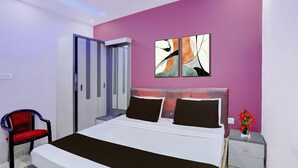A modern bedroom with a bed, a chair, a nightstand, and abstract wall art. - Suitehotel Aman Inn (Sitapur)