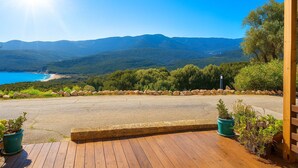 A wooden deck with potted plants, a paved area, and a scenic view of a coastal landscape with mountains in the background. - Magnifique duplex vue mer avec clim, wifi, piscine, mer à pied (Serra-di-Ferro)