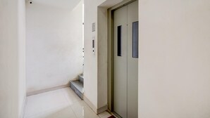 A hallway with a door, a light switch, and a small step leading to an elevator. - Hotel O Oragadam Industrial Estates Chennai (Walajabad)
