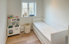 A child's bedroom with a bunk bed, a desk with toys, a window, and a radiator.