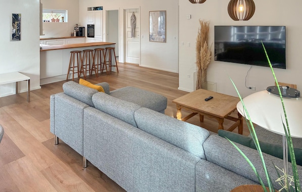 A modern living room with a sectional sofa, a TV, and a kitchen area in the background.