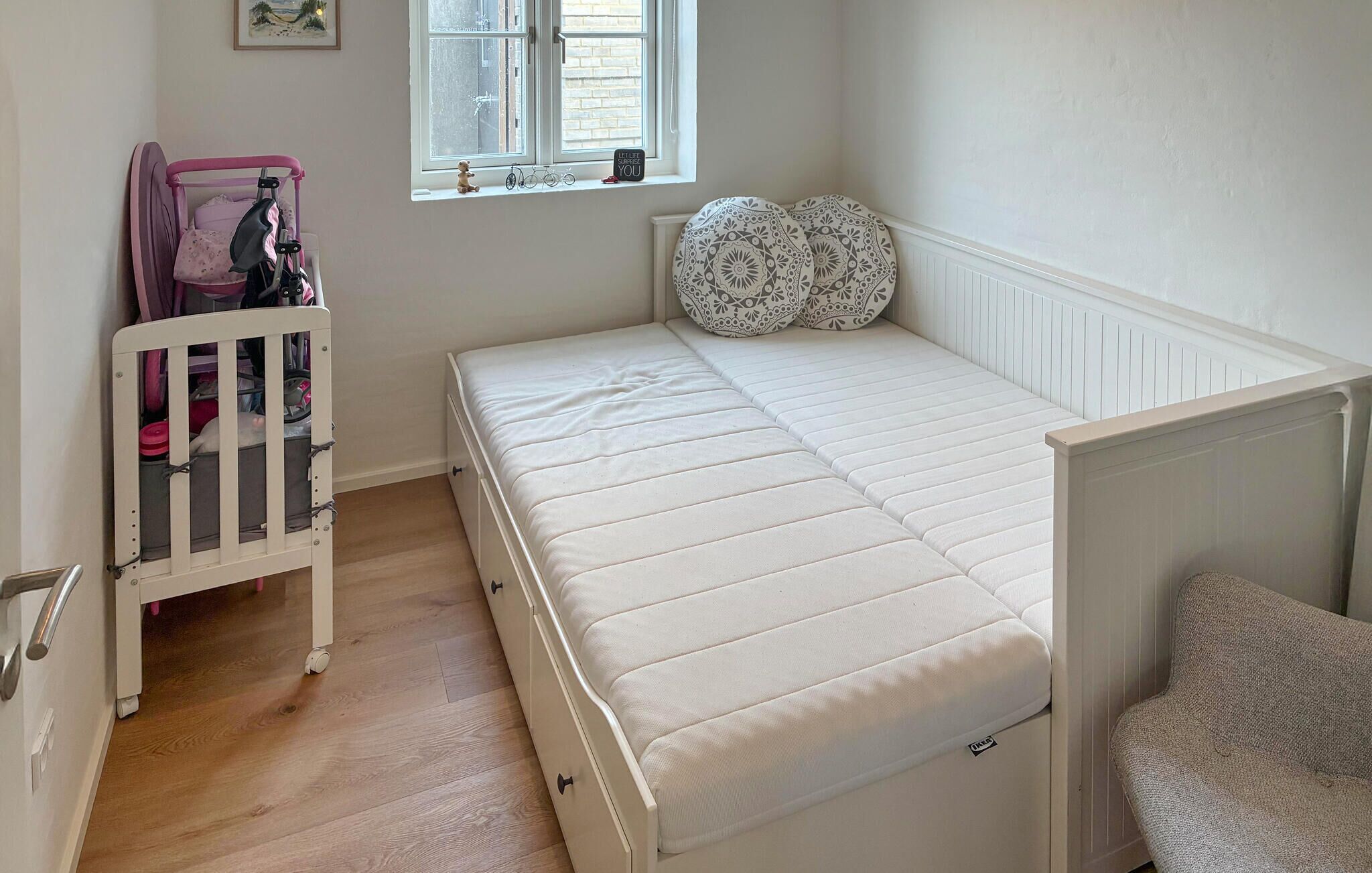 A room with a white bed, a crib, a window with a view, and a radiator.