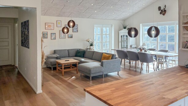 A modern kitchen with a wooden countertop, a grey sectional sofa, and a dining area with chairs and a table. - 4 bedroom lovely home in Malling (Malling)