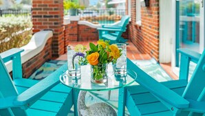 A glass table with a vase of flowers and two glasses on a patio with turquoise chairs. - Charmed Lagoon (Galveston)