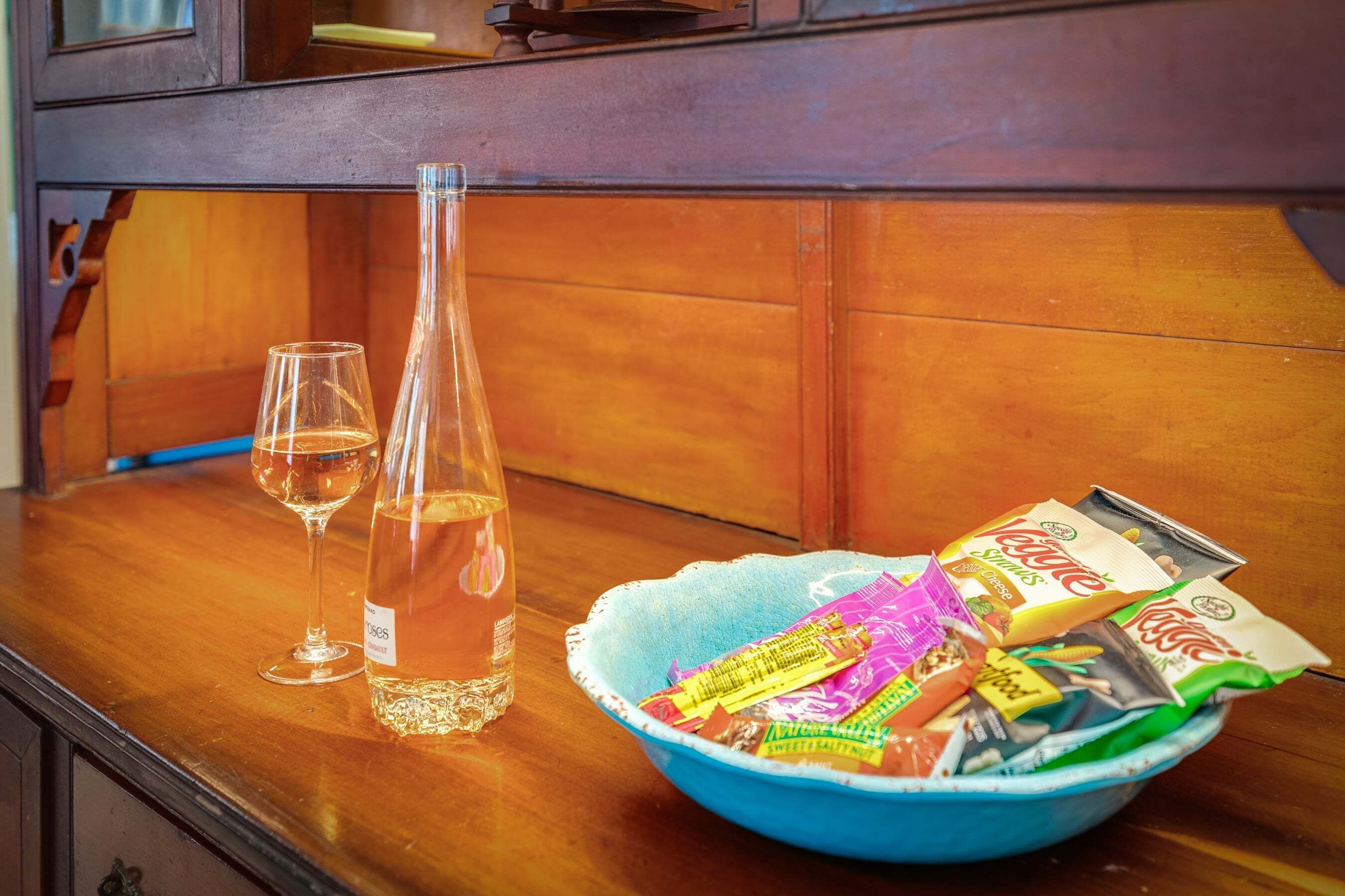 A wooden table with a clear bottle, two glasses, and a bowl of snacks.