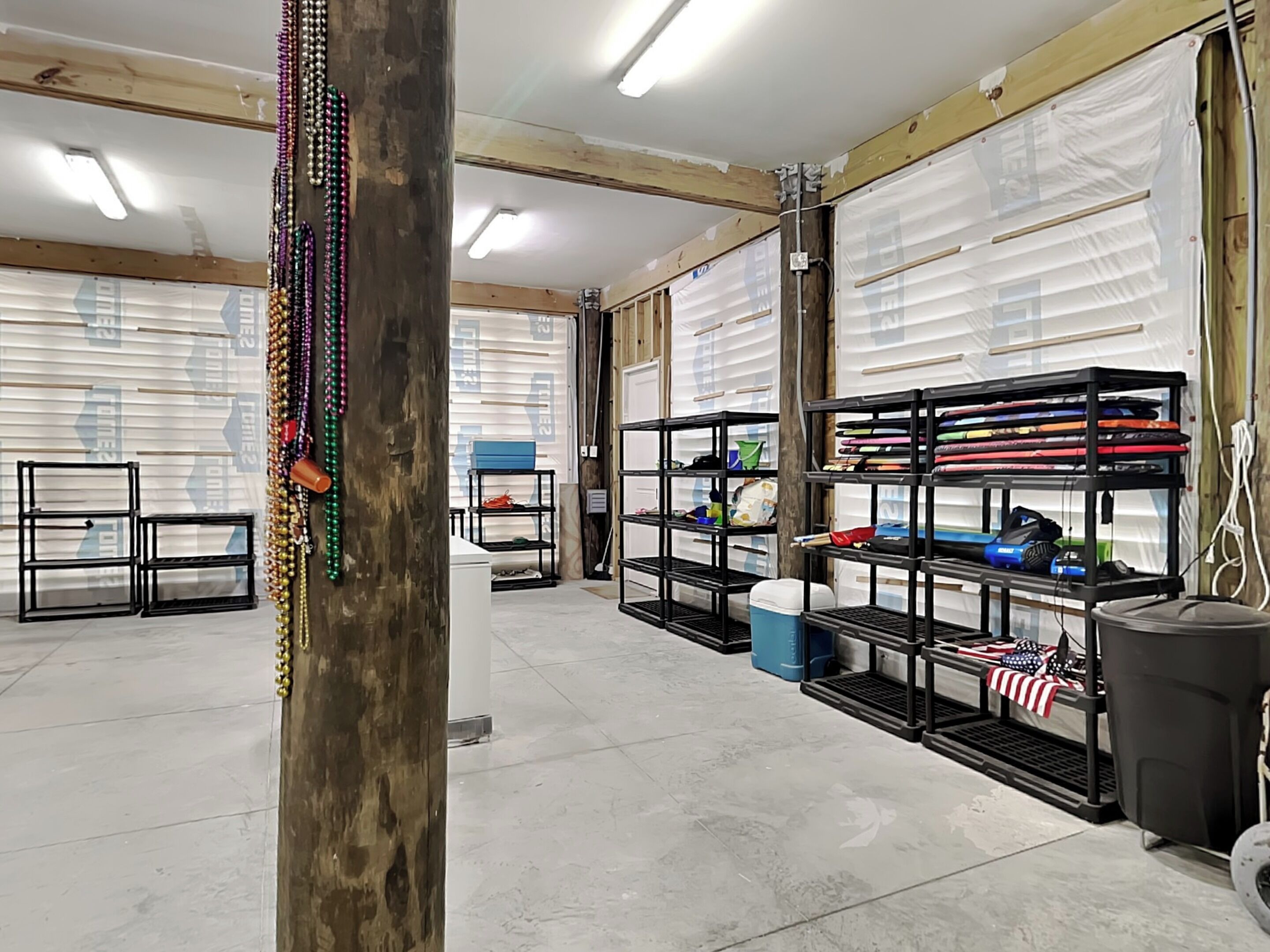 Un grand garage comprenant plusieurs établis, des étagères remplies d’outils et une grande poubelle.