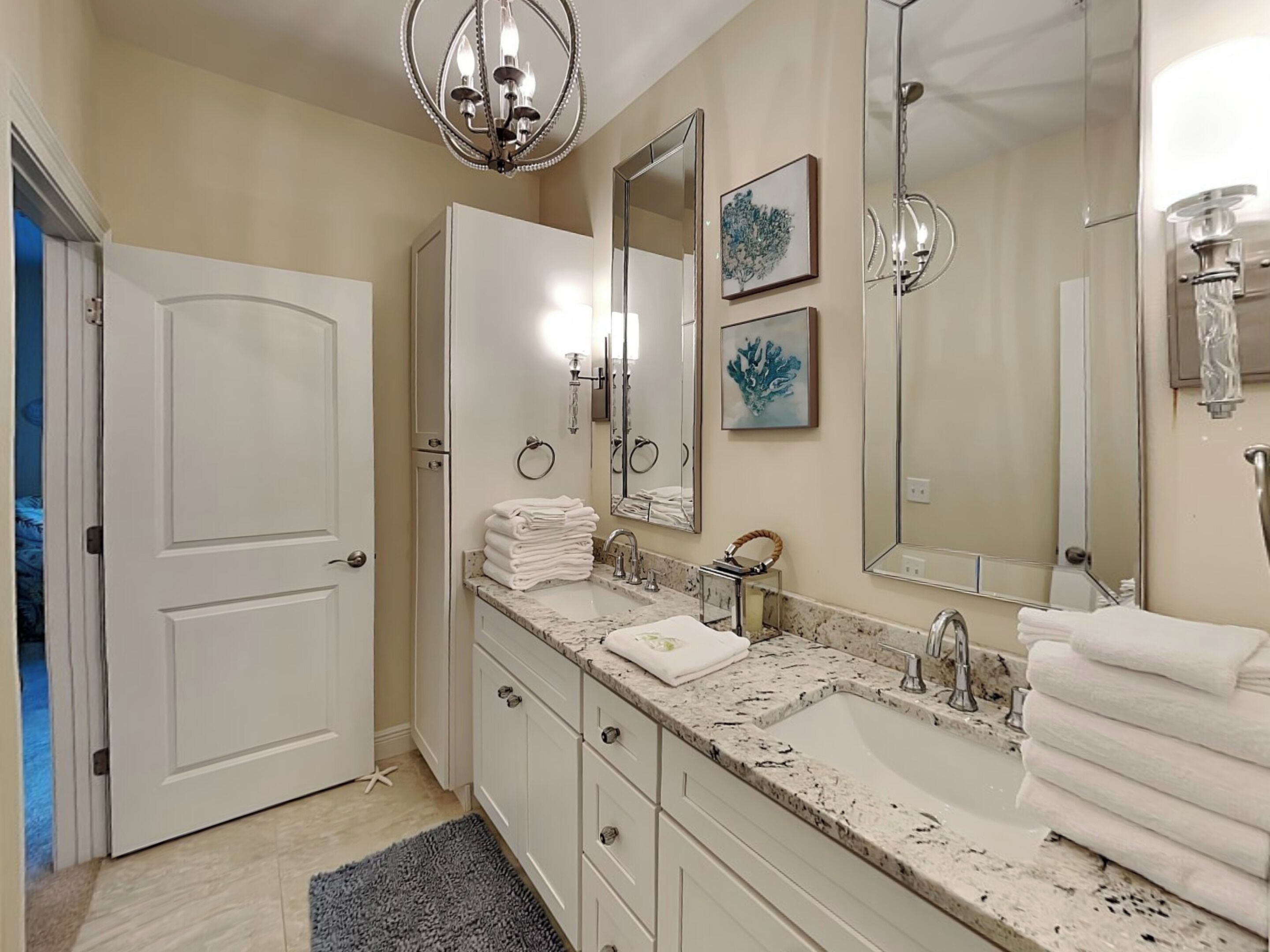 A bathroom with two sinks, a large mirror, and a chandelier.