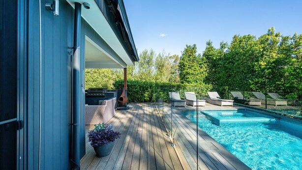 Eine Holzterrasse mit Pool, Liegestühlen und Grillplatz.