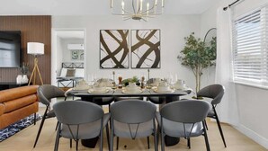 Un coin repas avec une table dressée pour six personnes, un lustre et deux œuvres d’art abstraites accrochées au mur.