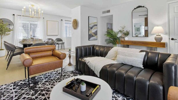 Un salon comprenant un canapé en cuir noir, un fauteuil en cuir marron, une table à manger avec des chaises, un lustre et un ventilateur de plafond.