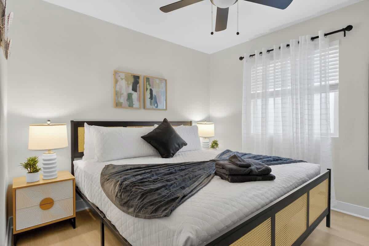 A bedroom with a bed, two bedside tables with lamps, a ceiling fan, and a window with curtains.