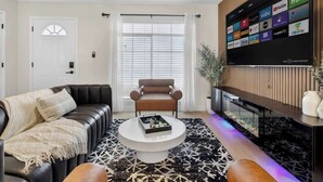 Un salon moderne avec un canapé en cuir noir, une table basse ronde et un téléviseur fixé au mur, au-dessus d’un meuble noir servant de support pour divers services de diffusion en continu.