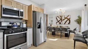 Une cuisine moderne dotée d’appareils électroménagers en acier inoxydable, de meubles en bois et d’un coin repas agrémenté d’un lustre.