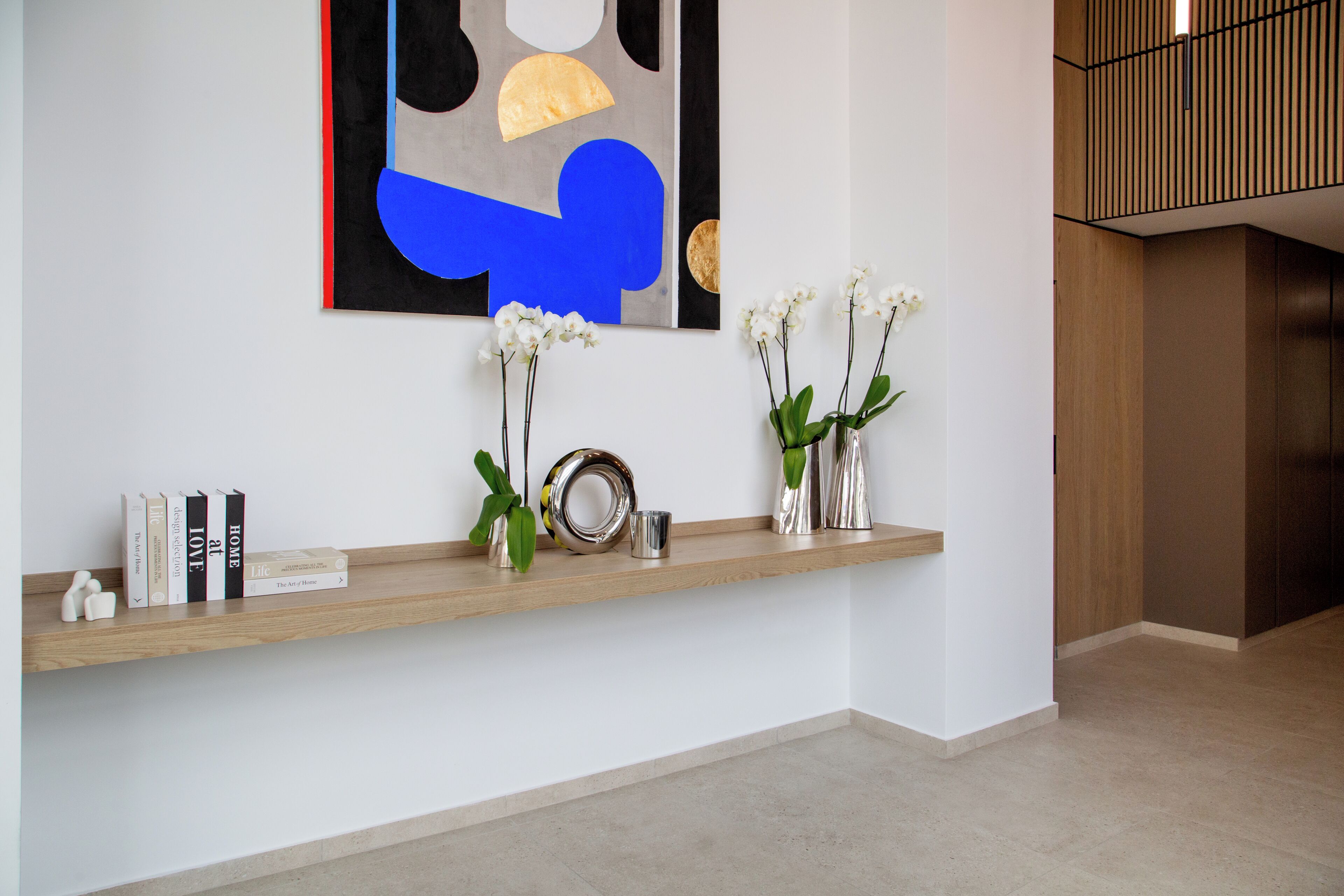 A modern interior with a wooden shelf displaying books, decorative items, and vases with flowers.