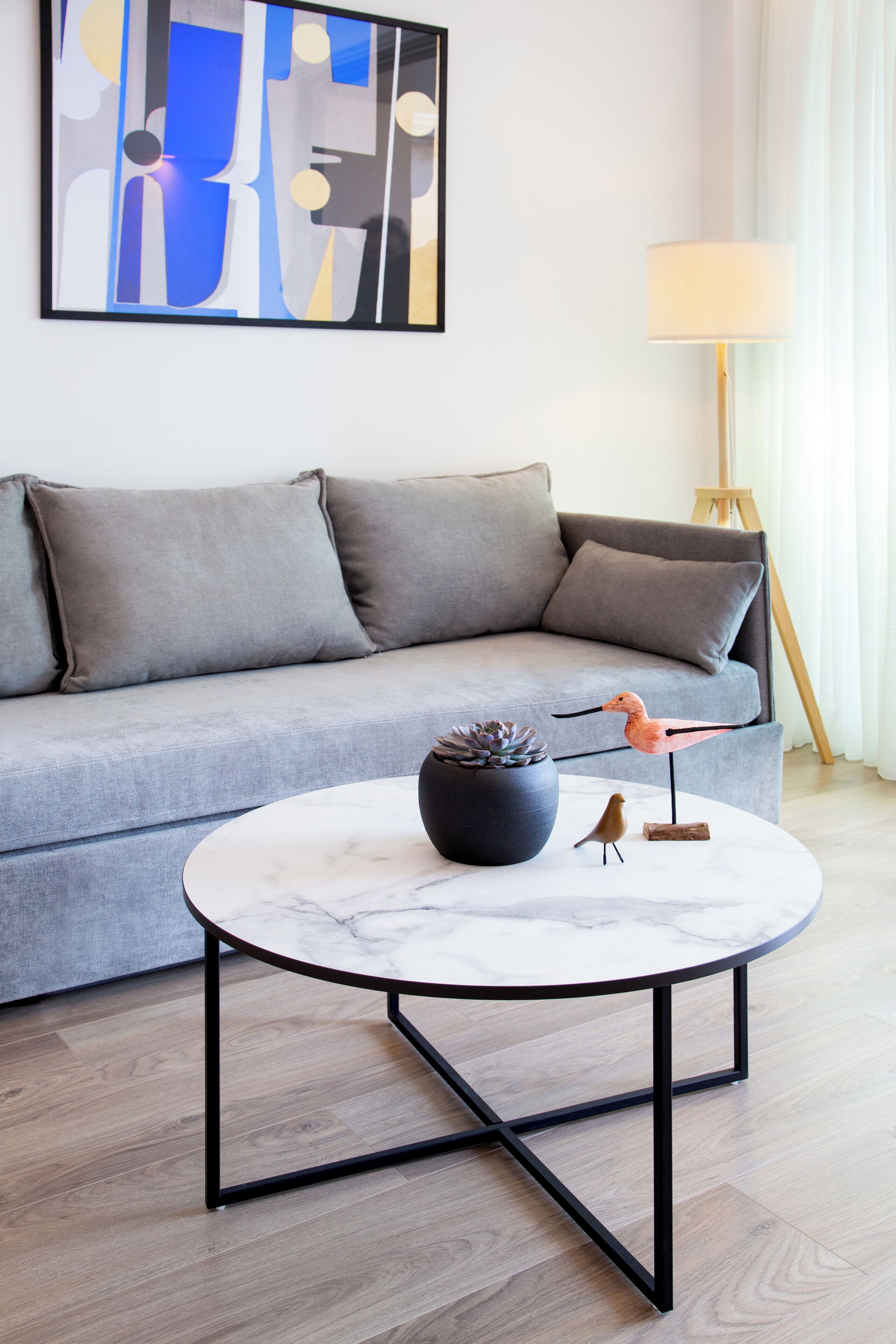 A modern living room with a grey sofa, a round marble coffee table, and a lamp.