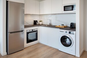 Una cocina compacta con refrigerador de acero inoxidable, horno empotrado, lavadora, microondas y un lavamanos pequeño.