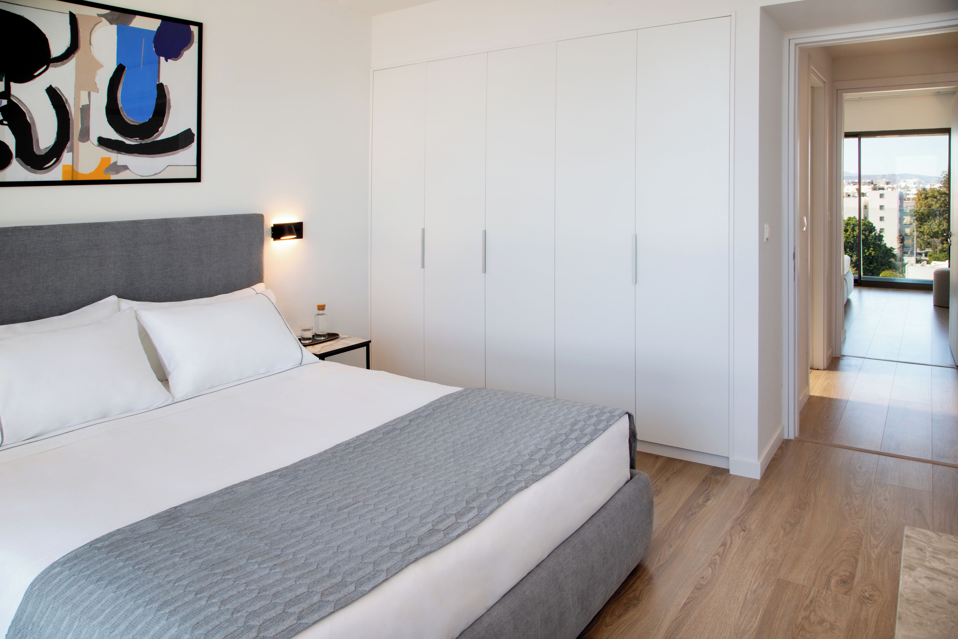 A bedroom with a bed, a nightstand, a wardrobe, and a view of the outside.