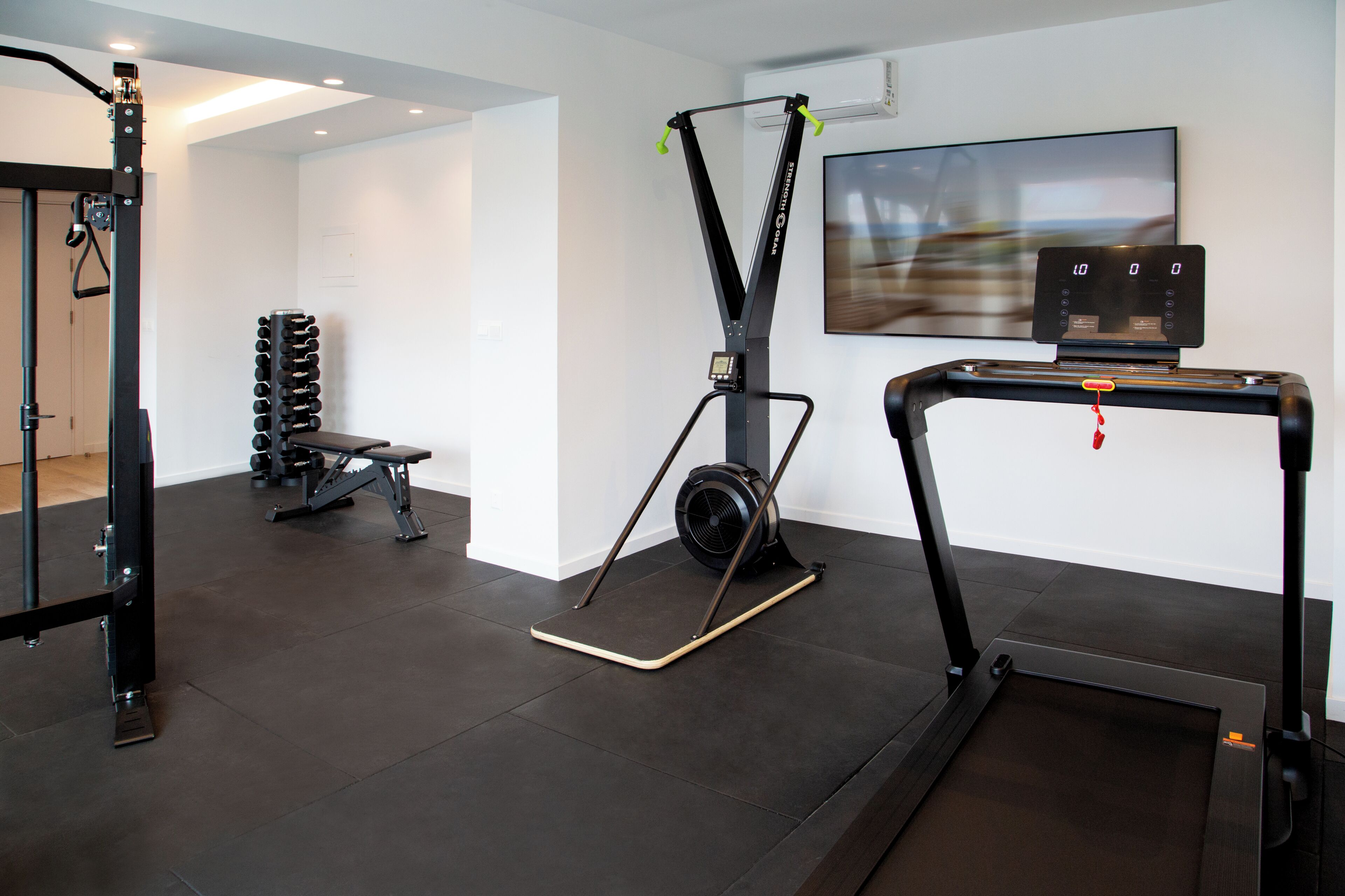 A gym with exercise equipment, a bench, and a wall-mounted TV.