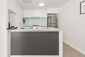 Eine kompakte Küche mit weißen Schränken, einem Edelstahlkühlschrank und einem eingebauten Backofen.
