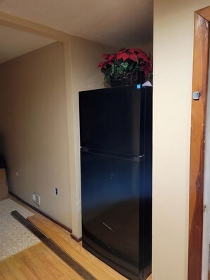 A black refrigerator in a room with beige walls and a wooden floor. - Historic Farm House & Barn in Quaint Wolcott NY 1 mile from Lake Ontario (Wolcott)