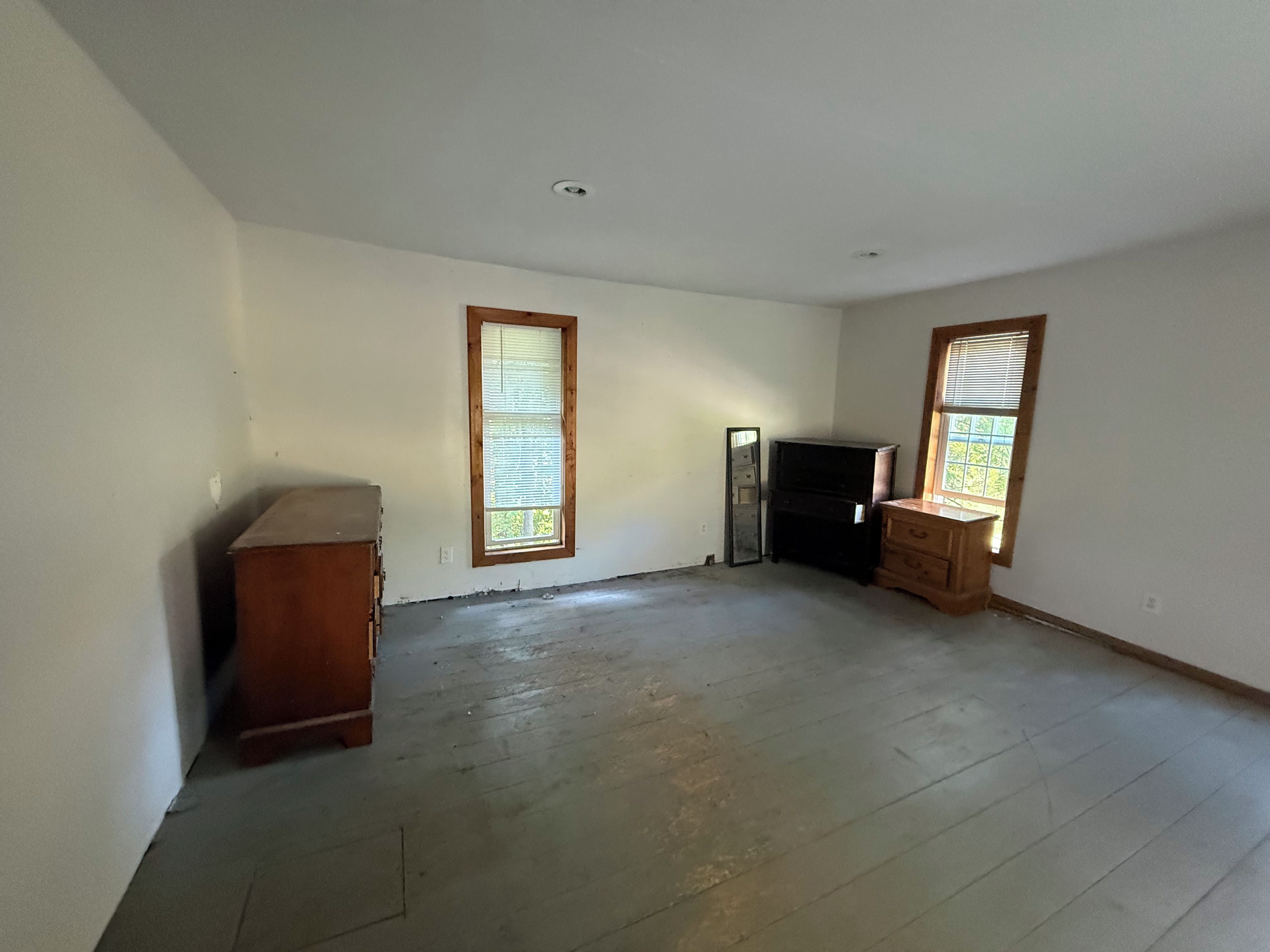 A room with two windows, a wooden dresser, and a black cabinet.