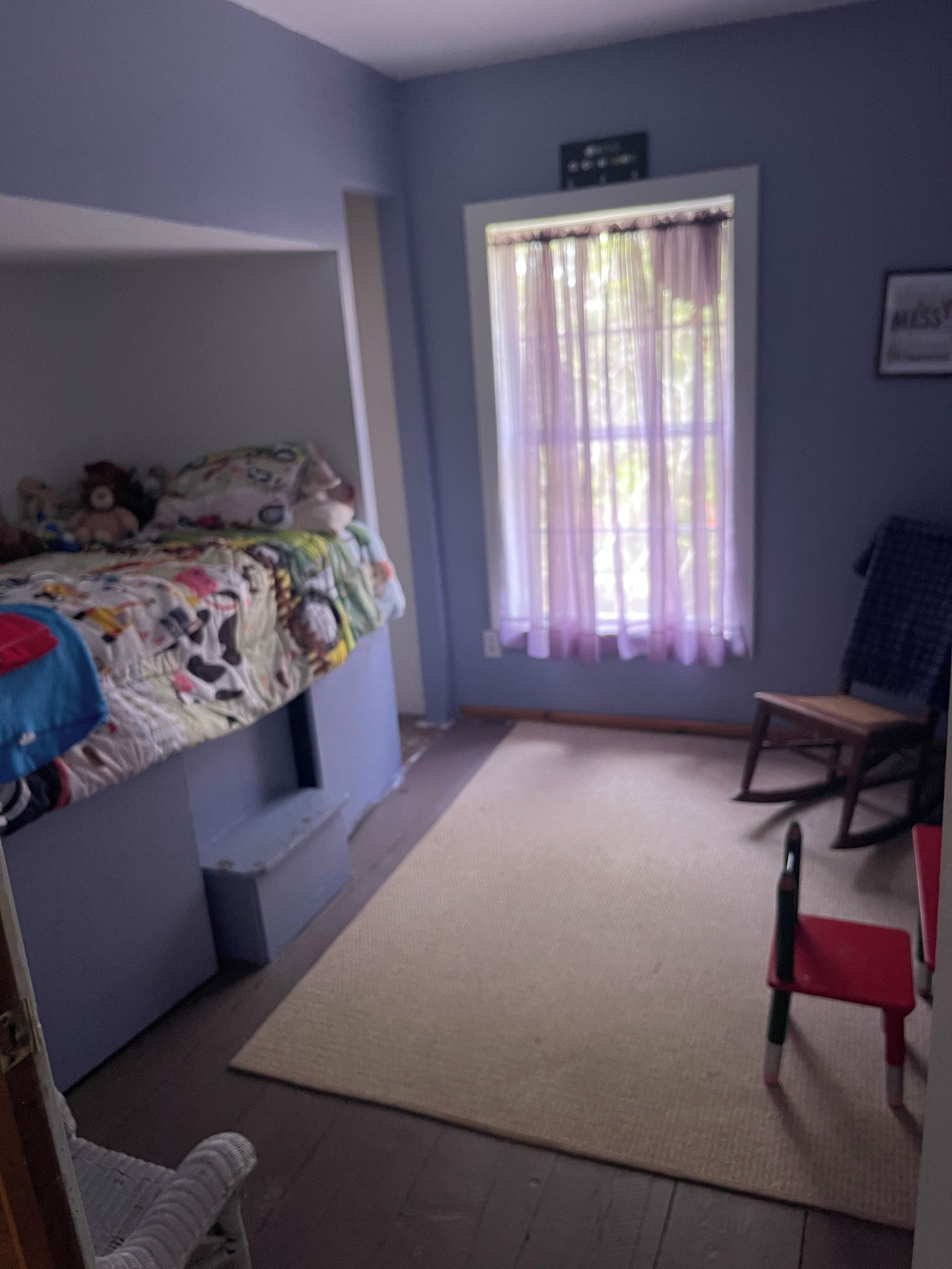 A room with a bunk bed, a desk, a chair, and a window with curtains.