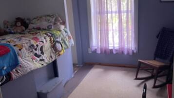 A room with a bunk bed, a desk, a chair, and a window with curtains.