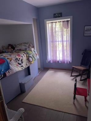 A room with a bunk bed, a desk, a chair, and a window with curtains.