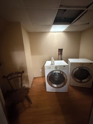 A laundry room with two washing machines, a chair, and a power outlet on the wall.