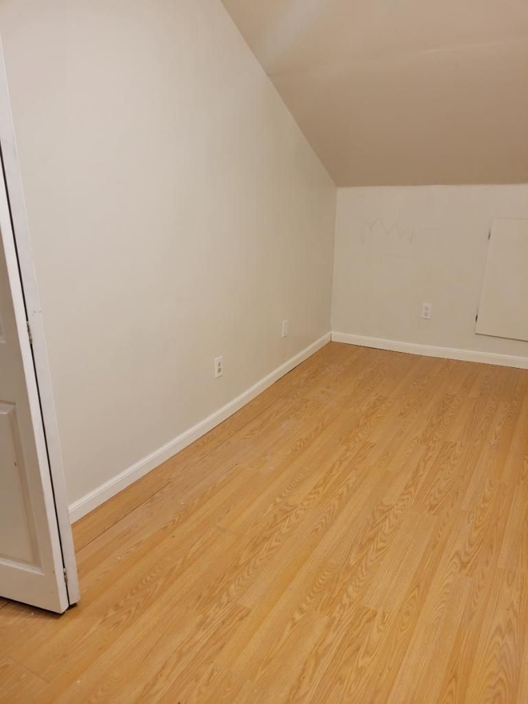 A room with wooden flooring, white walls, and a door on the left.