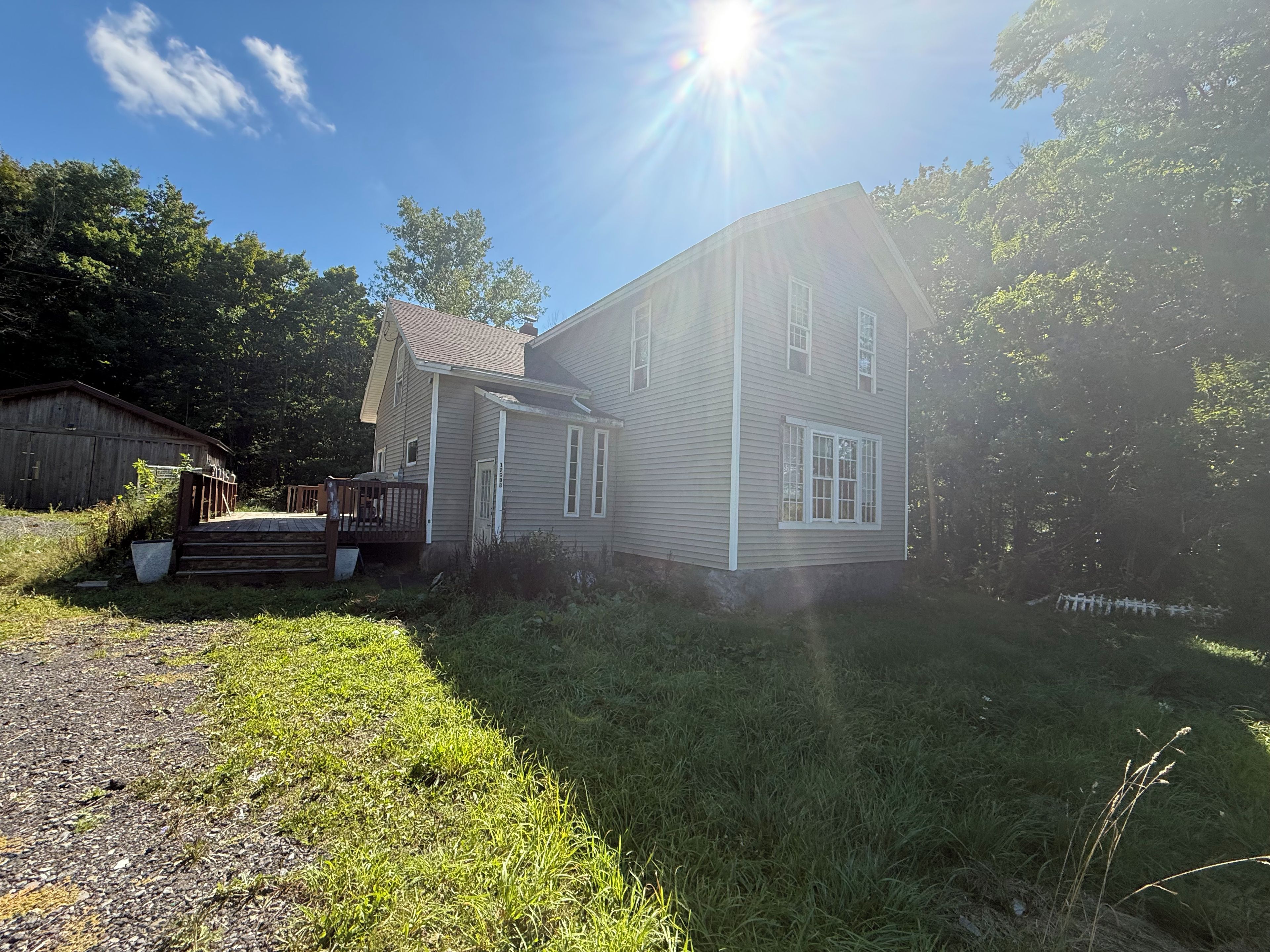 A two-story house with a front porch and a small deck, surrounded by a grassy yard and trees.