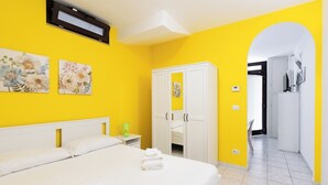 Een hotelkamer met een bed, een kledingkast, een nachtkastje en een deur naar een andere kamer.